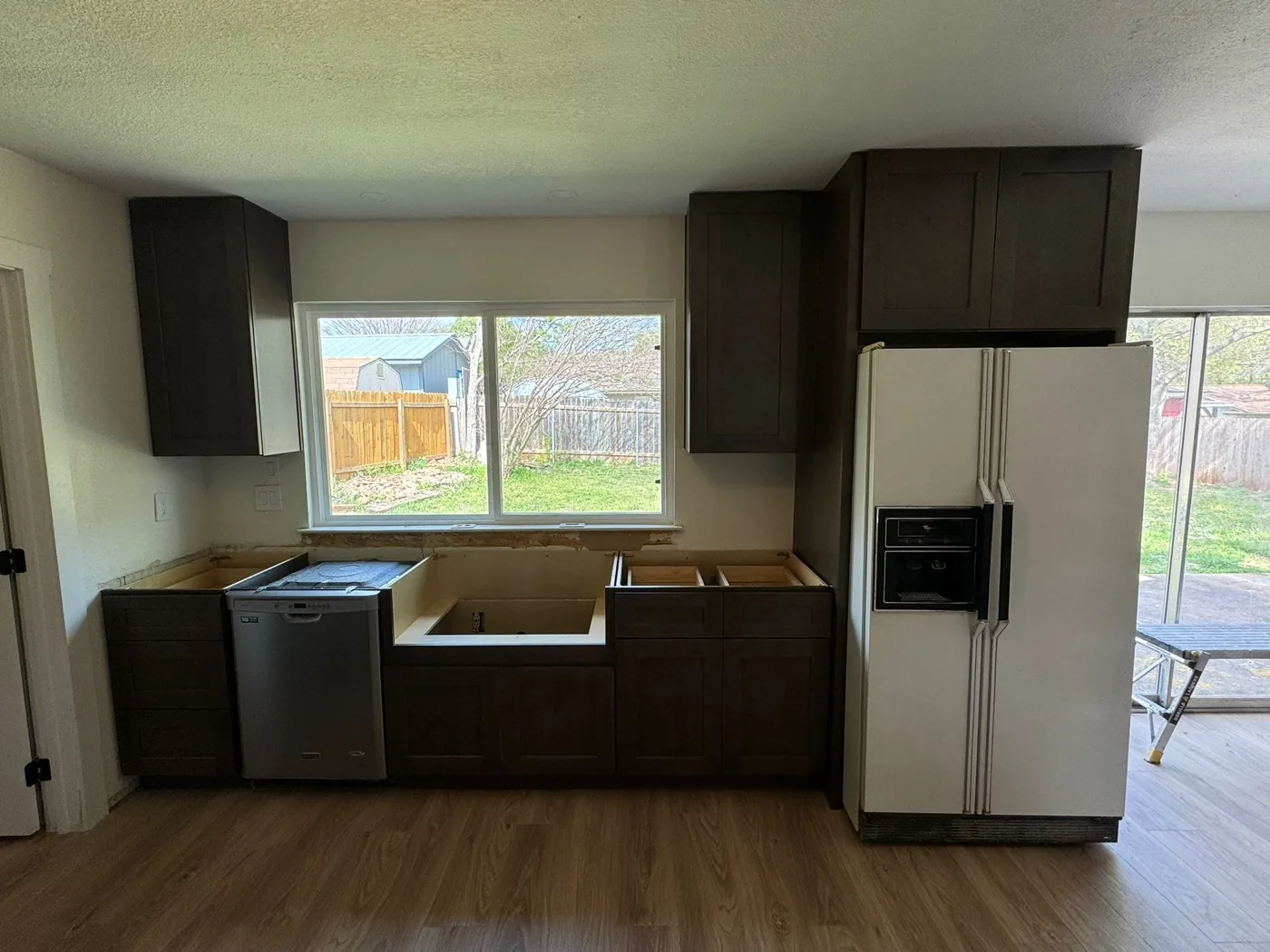 Dark brown Shaker cabinets set around a stainless dishwasher and an older white side-by-side refrigerator, before the countertop goes on